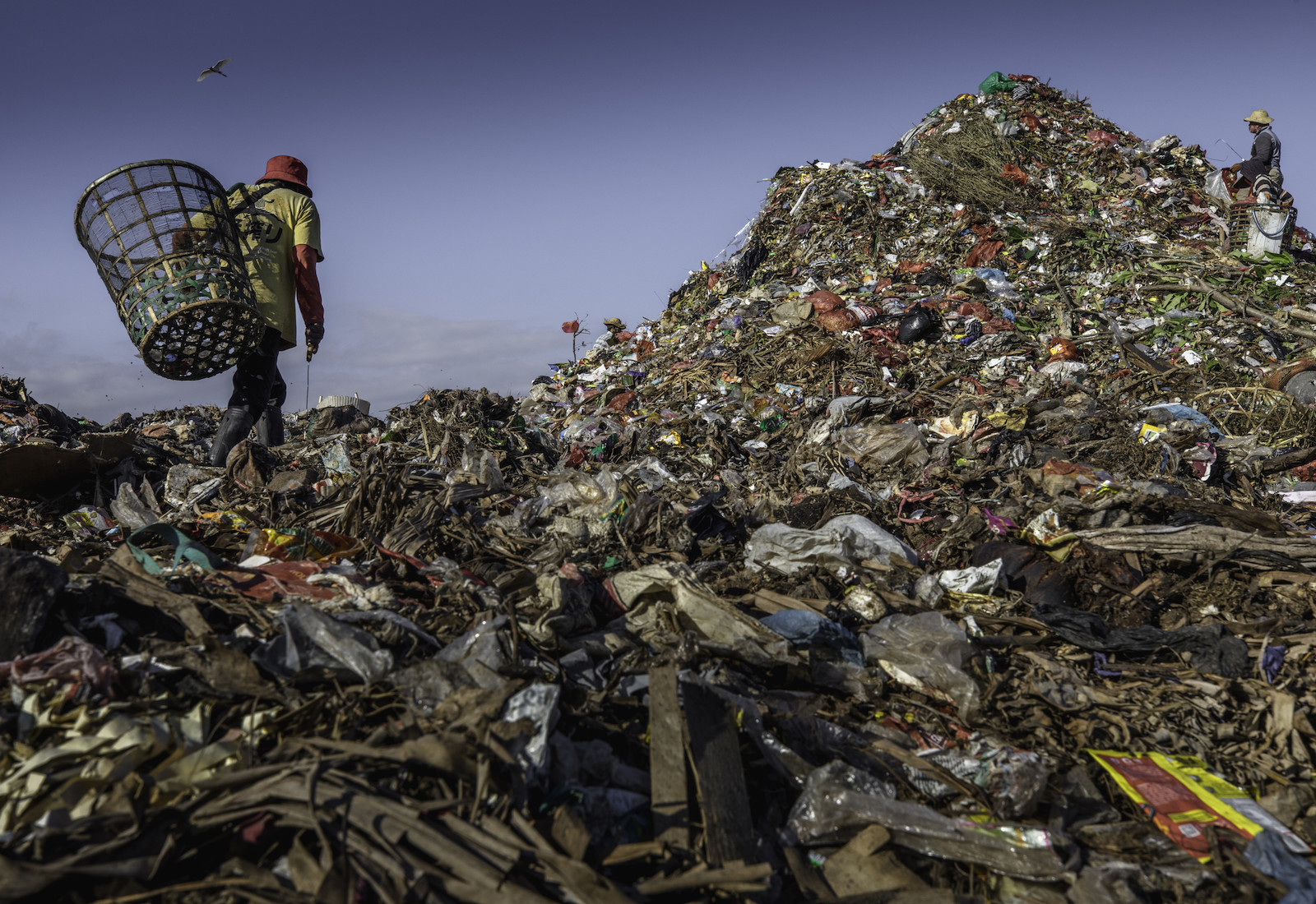 Two people with baskets collecting garbage on a mountain of trash