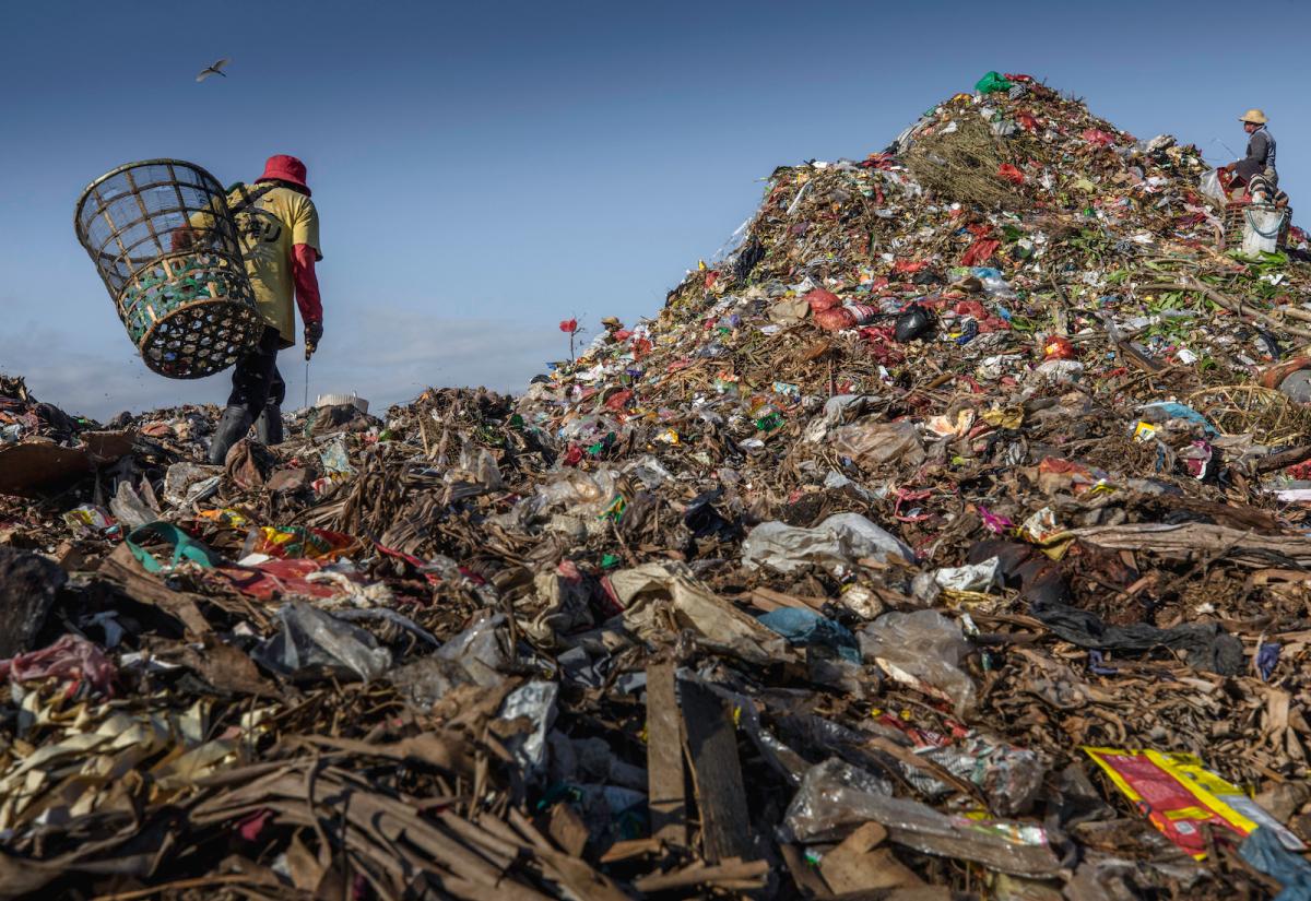 Two people with baskets collecting garbage on a mountain of trash