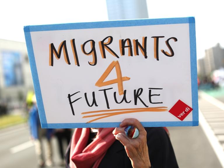 a hand holds up a sign that says "migrants 4 future"