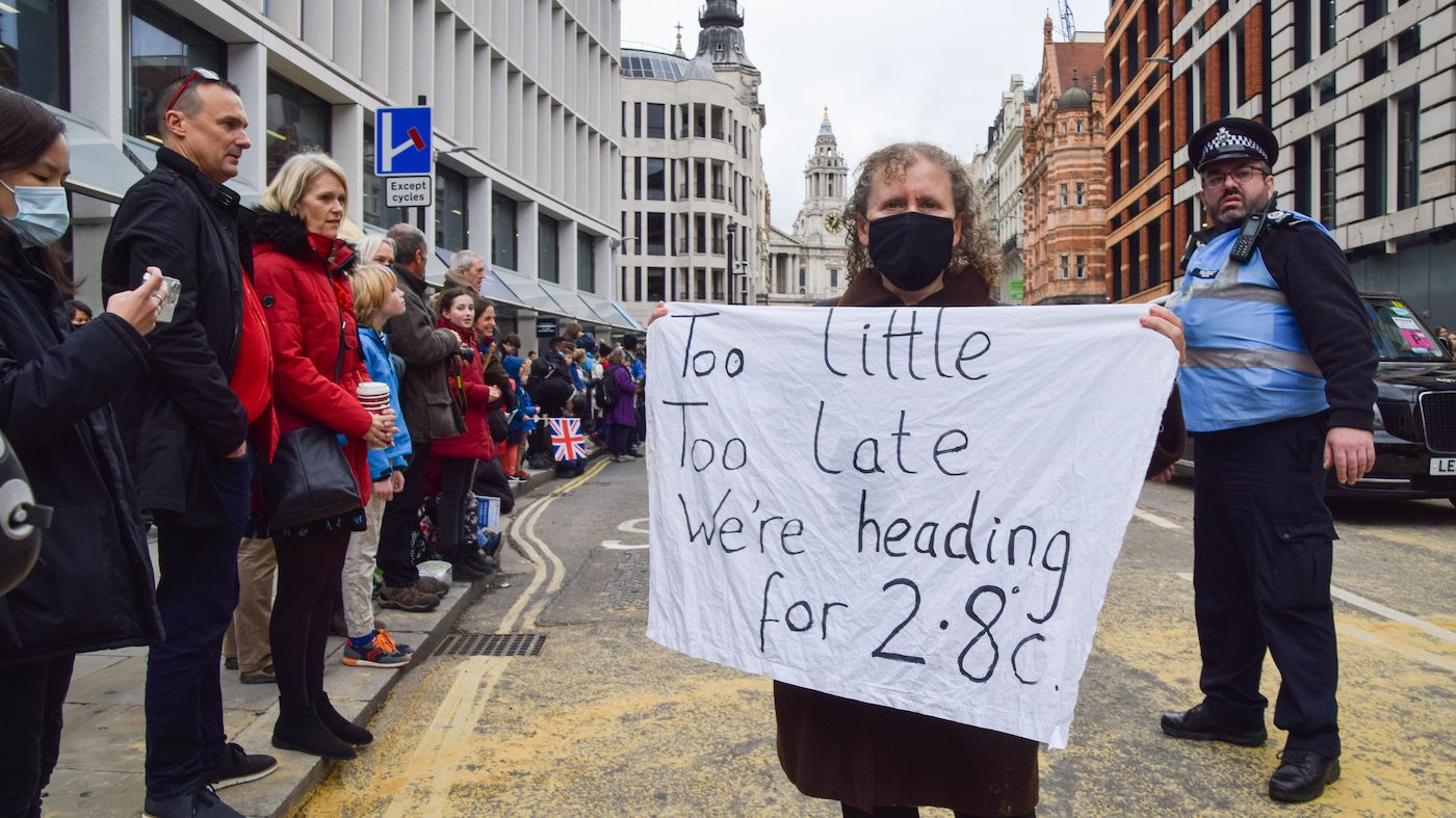 Woman holds sign that says "too little too late we're heading for 2.8"