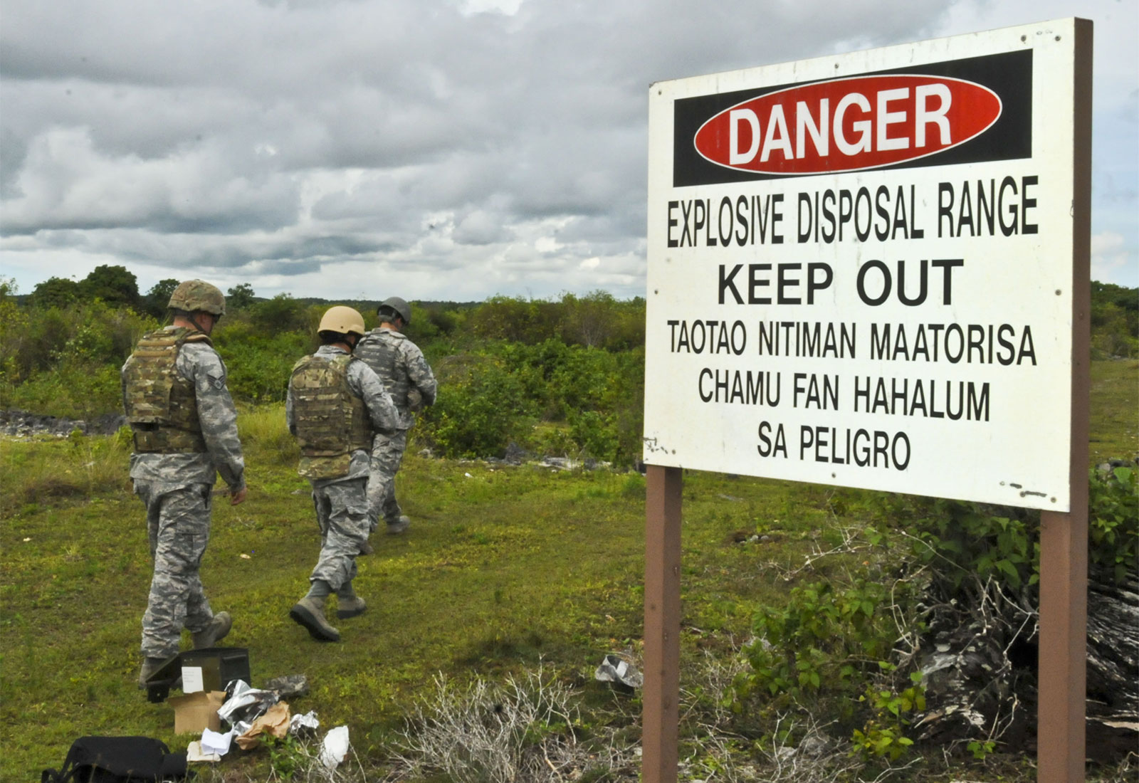 Three people in US Air Force uniforms walking past a sign warning of an explosive disposal range