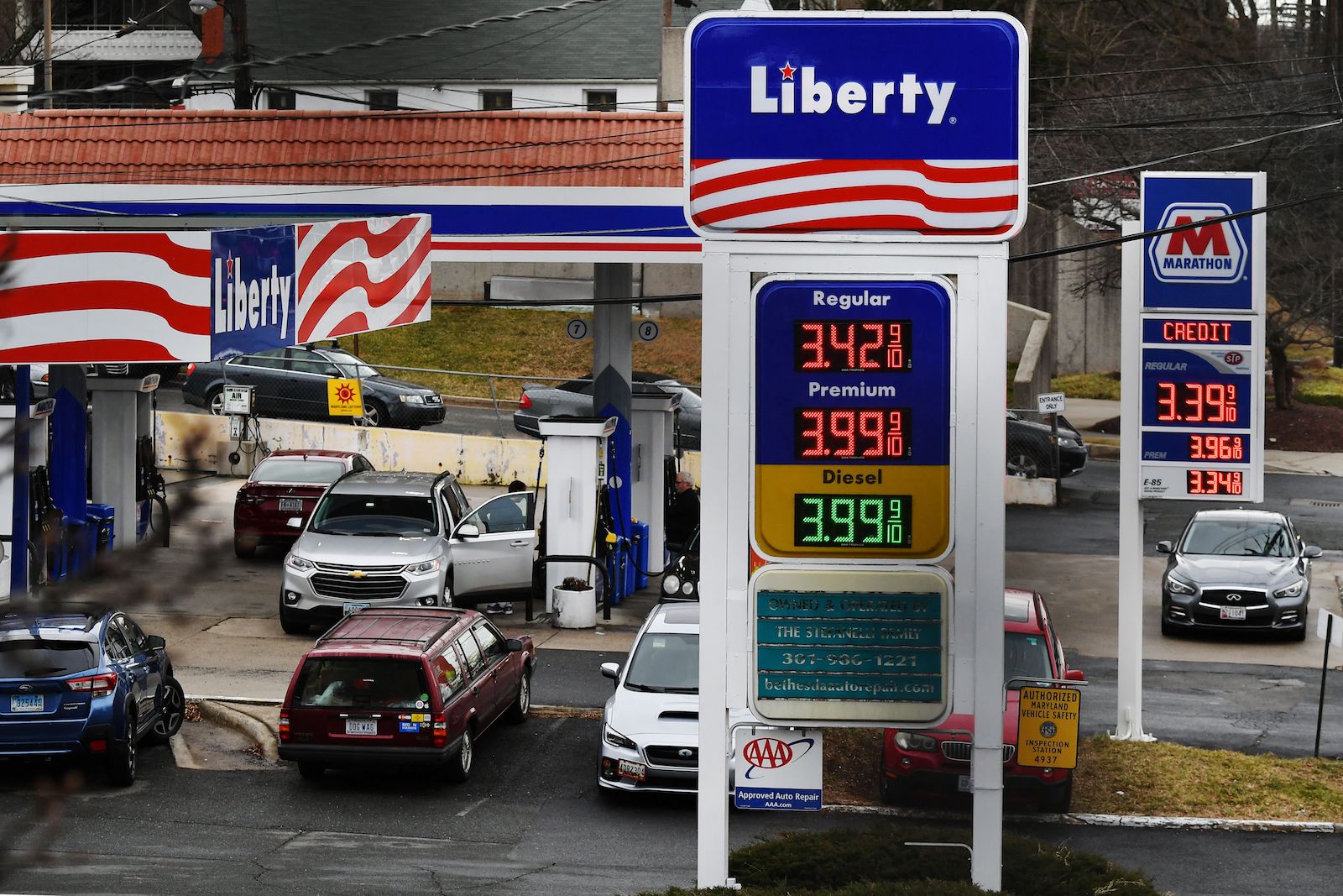 a gas station sign that says "liberty" with a flag motif shows prices while cars fuel up