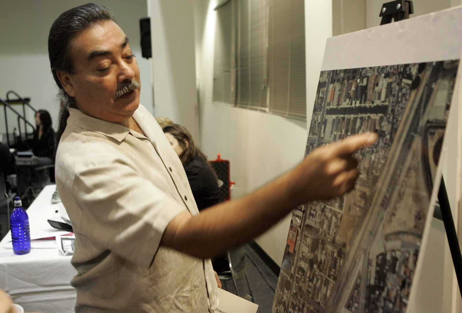 a man in a button-up shirt points to a printed aerial photo of a city