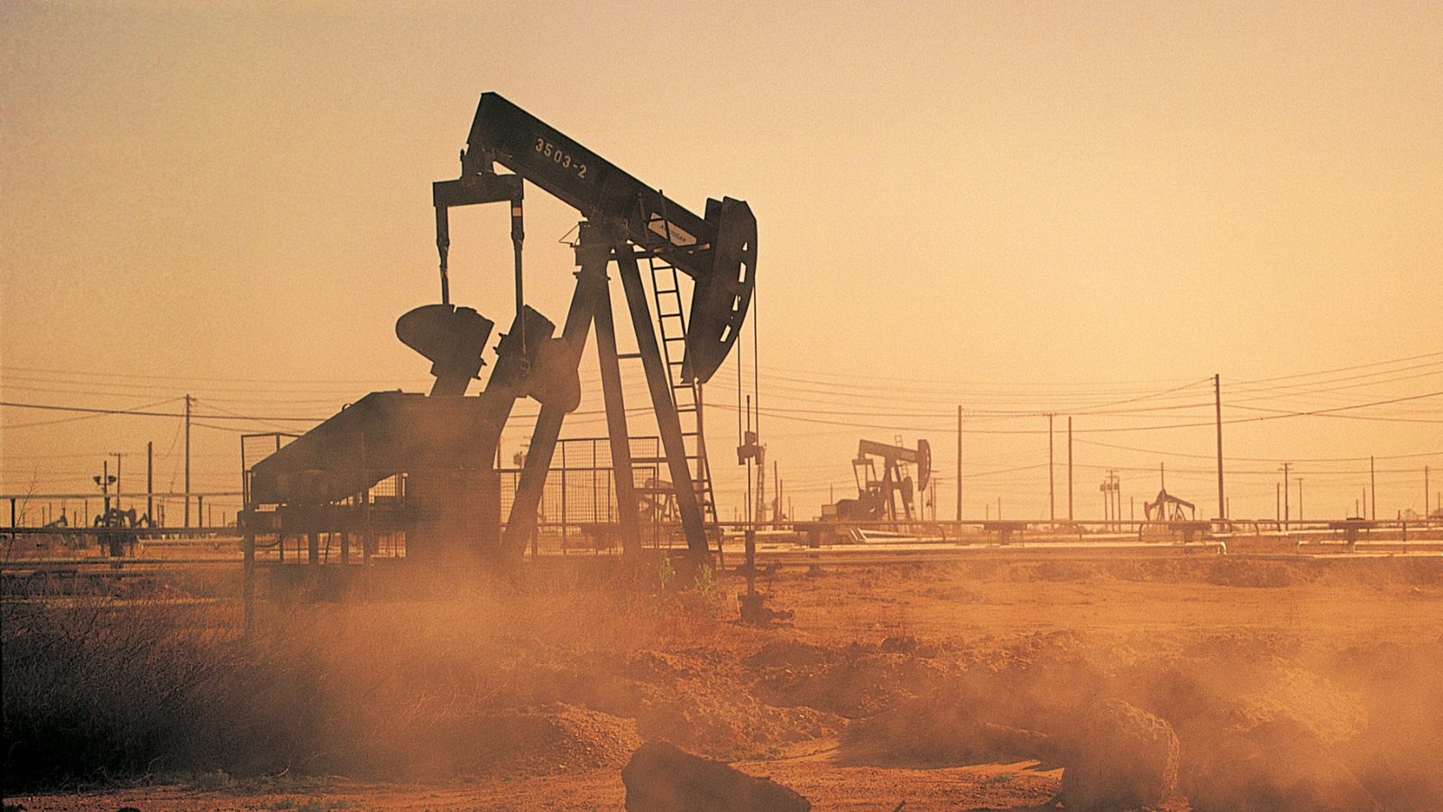 an oil pump jack in a dusty landscape against an orange sky