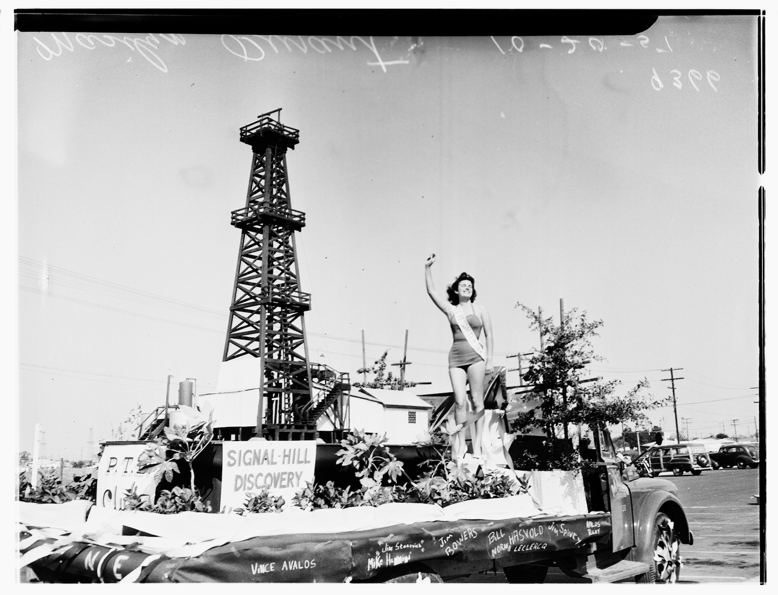 a black and white old photo of a woman on top of a parade float shaped like an oil well