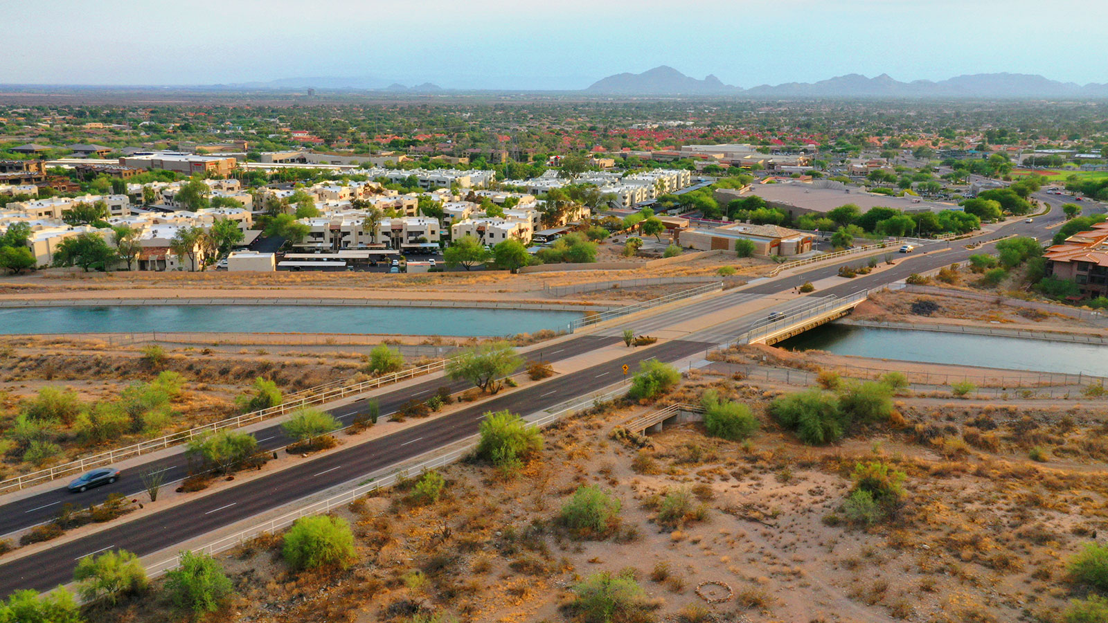 Scottsdale, Arizona highway over a river with buildings, green trees, and mountains in the distance