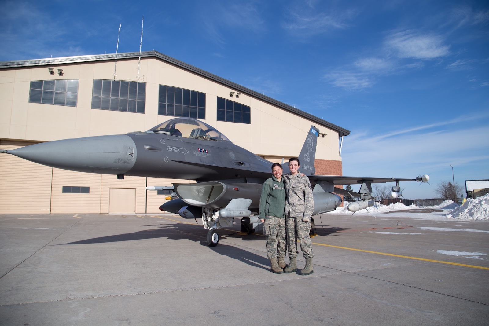 Two women in US Air Force Uniforms stand in front of an F-16 fighter jet