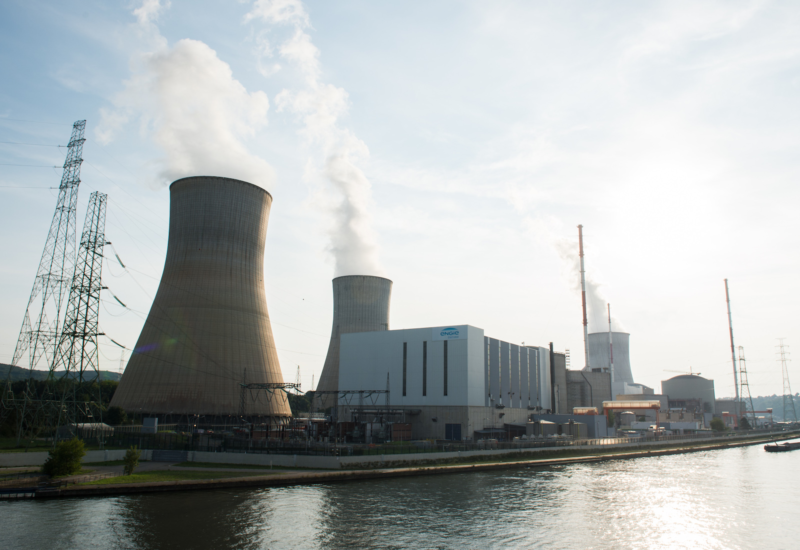 Three nuclear cooling towers on a river, with steam blowing from them
