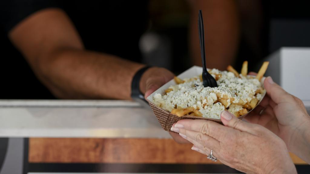 A server hands a takeout container with a plastic fork sticking out of it to a woman