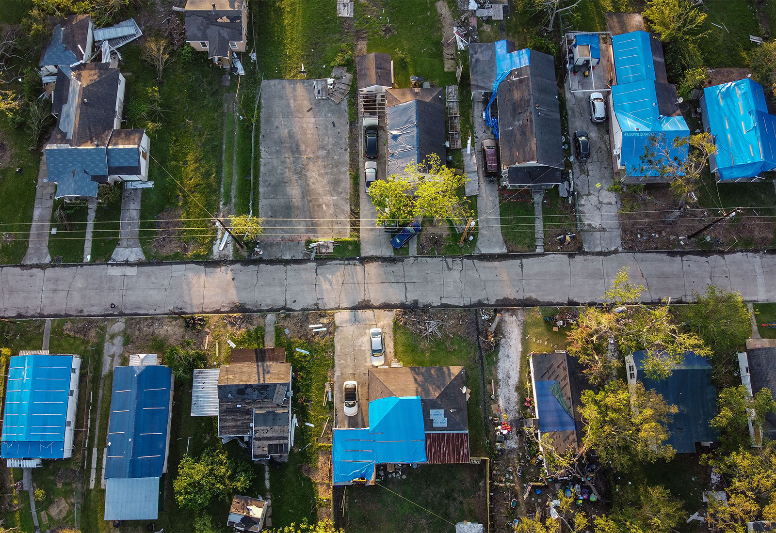 Aerial view of houses showing damage from a hurricane, most houses have blue tarps on the roofs