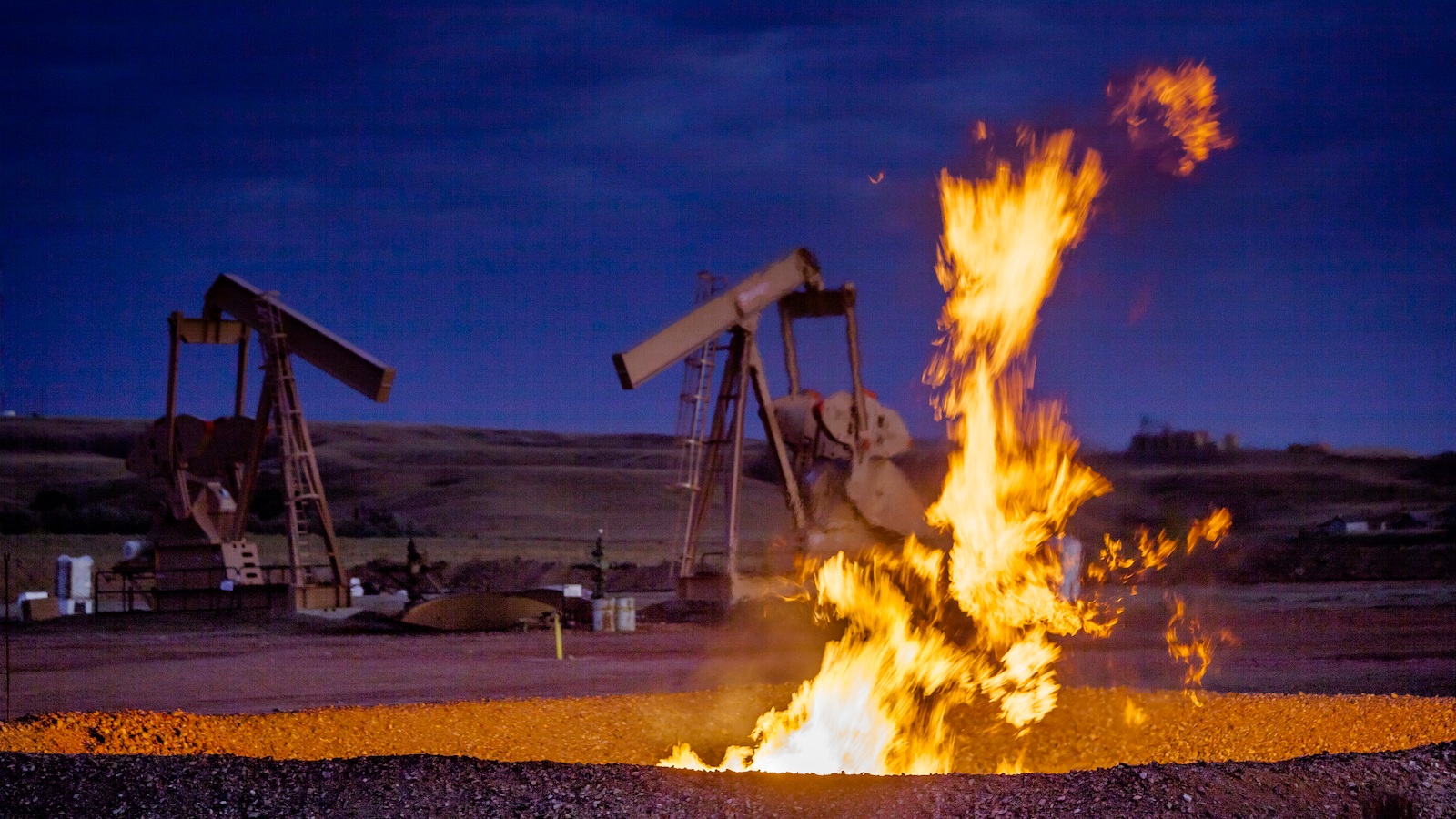 Flames emerge from a pit, with pumpjacks and a dark sky in the background.