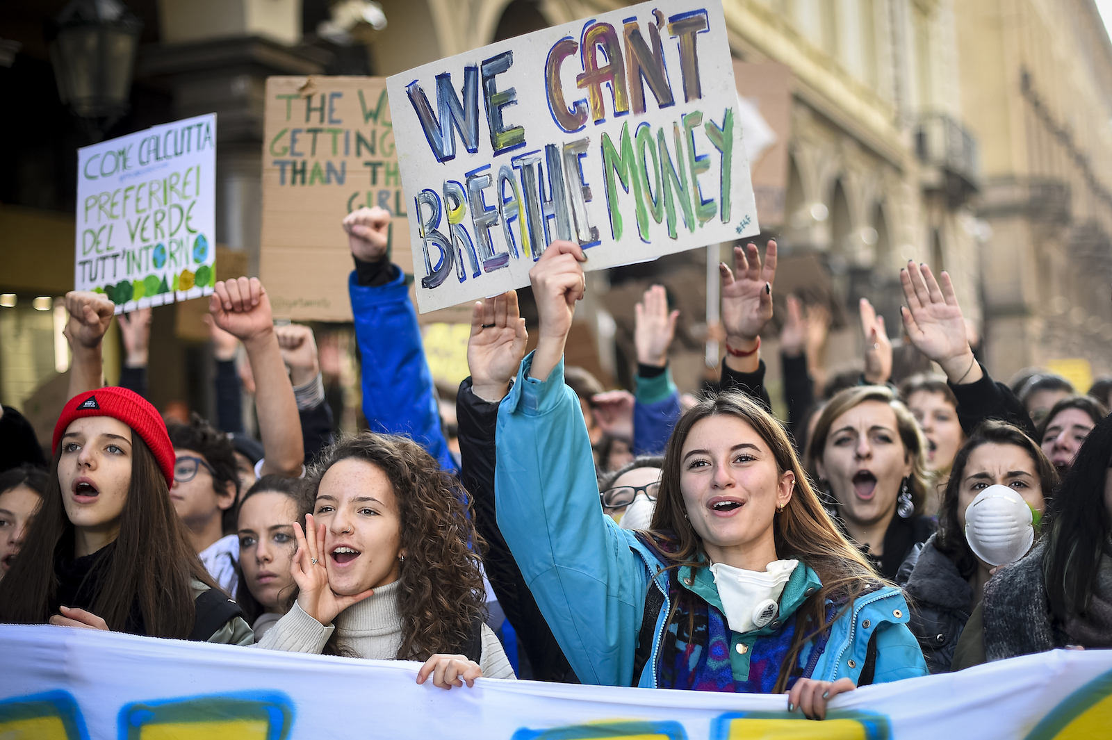 a girl in a green jacket holds a sign saying we can't breathe money during an outdoor protest