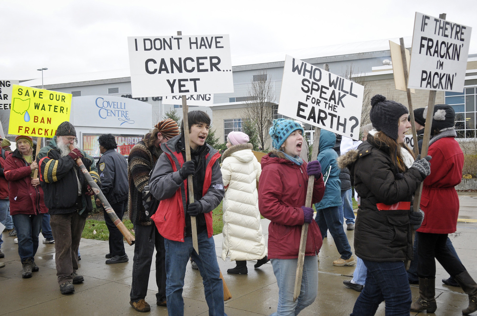 A group of protesters carry signs saying "I don't have cancer yet" and "Who will speak for the Earth"?