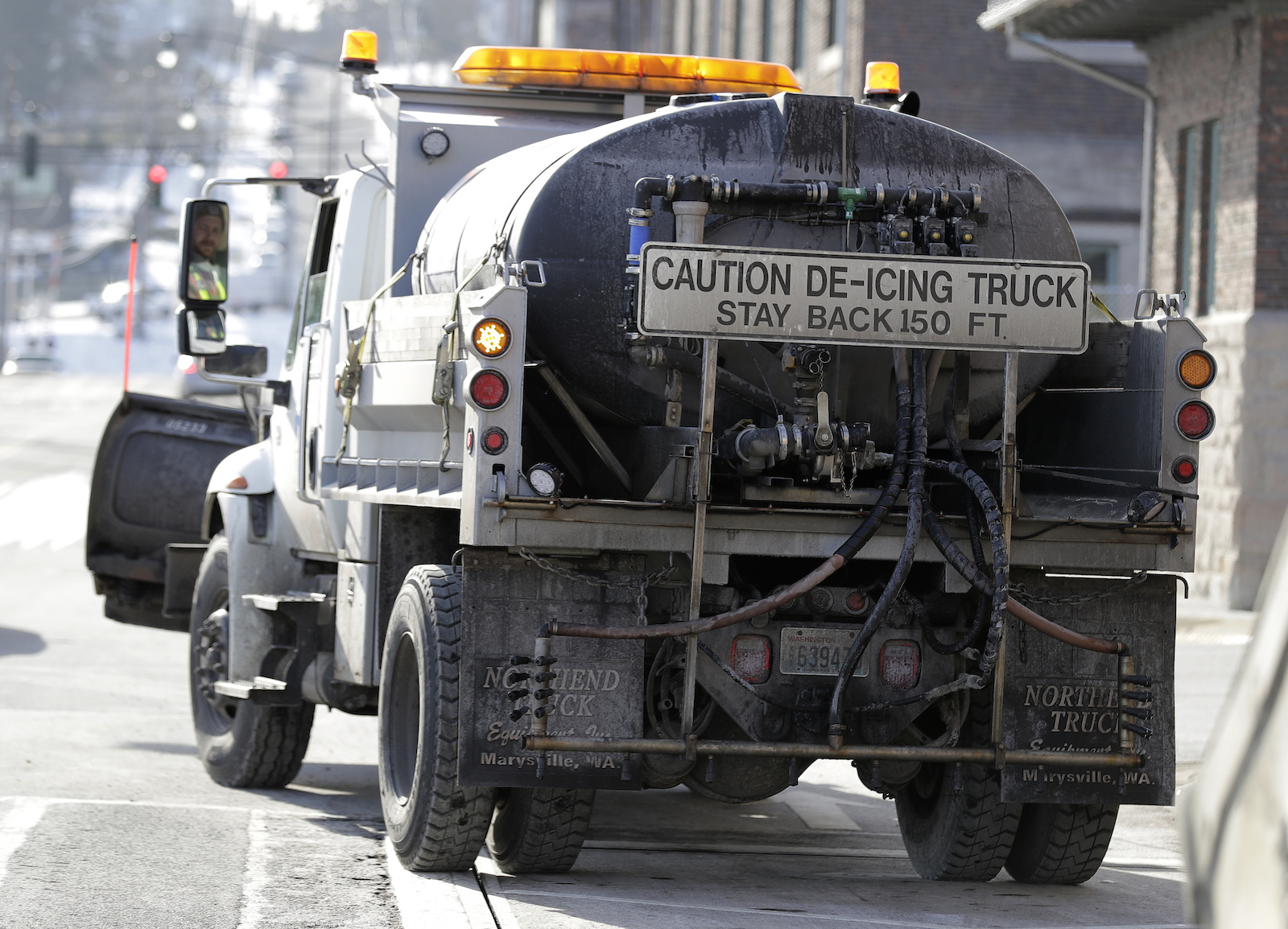 A truck with a sign that says "caution de-icing truck" drives down a street.