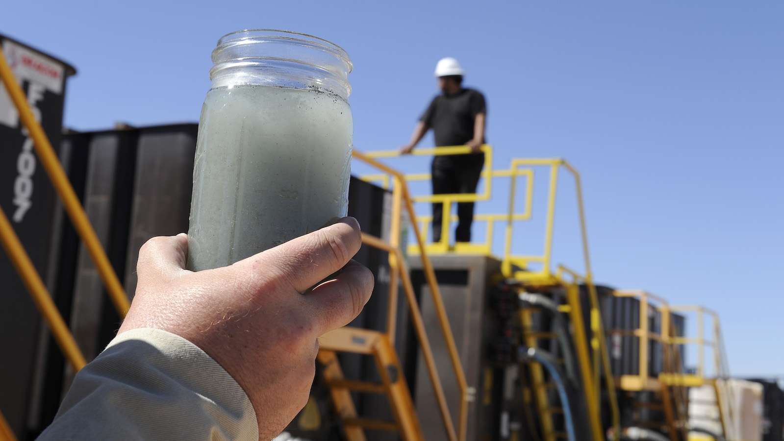 A jar holding grayish waste water from hydraulic fracturing is held up to the light at a recycling site.