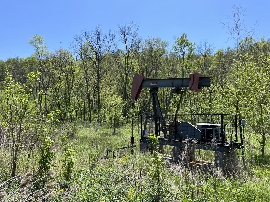An oil rig stands in a field surrounded by trees and green grass.
