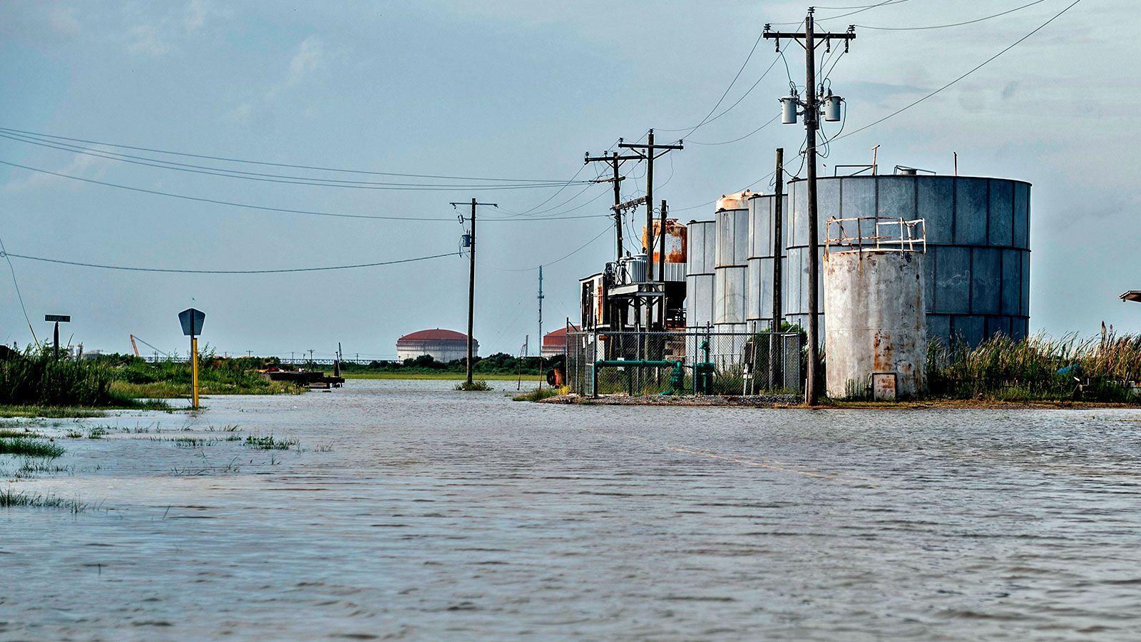 A flooded street with power lines and liquefied natural gas tanks in Cameron, Louisiana