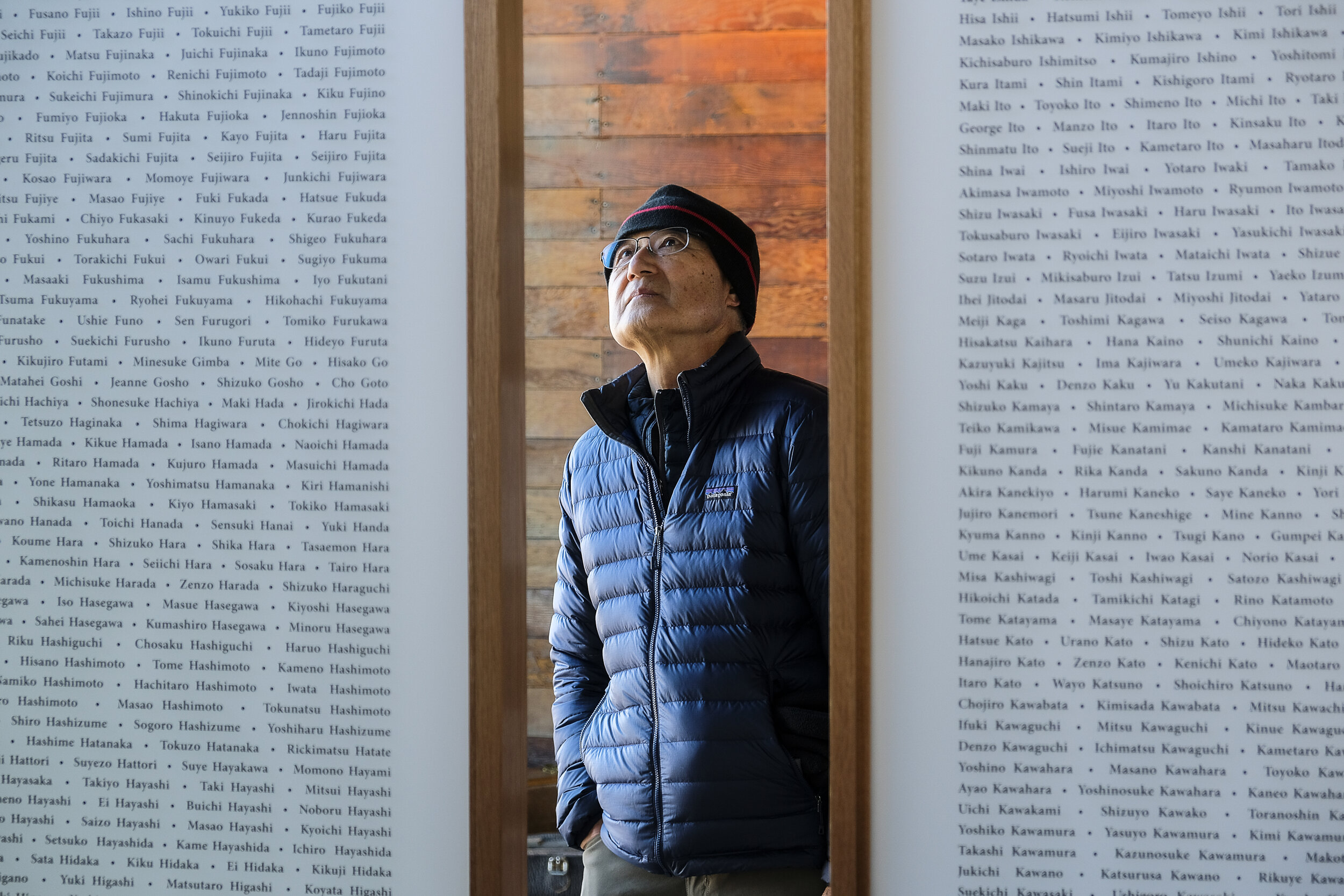 A man wearing a beanie and jacket looks up to read two large plaques filled with names.