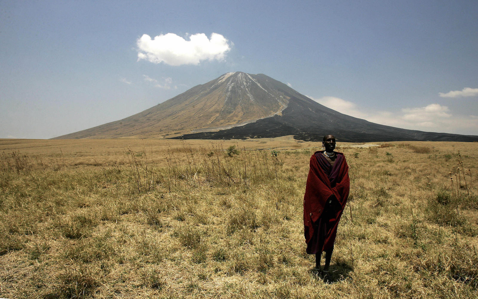 Maasai person stands on a grassy plain in front of a tall mountain
