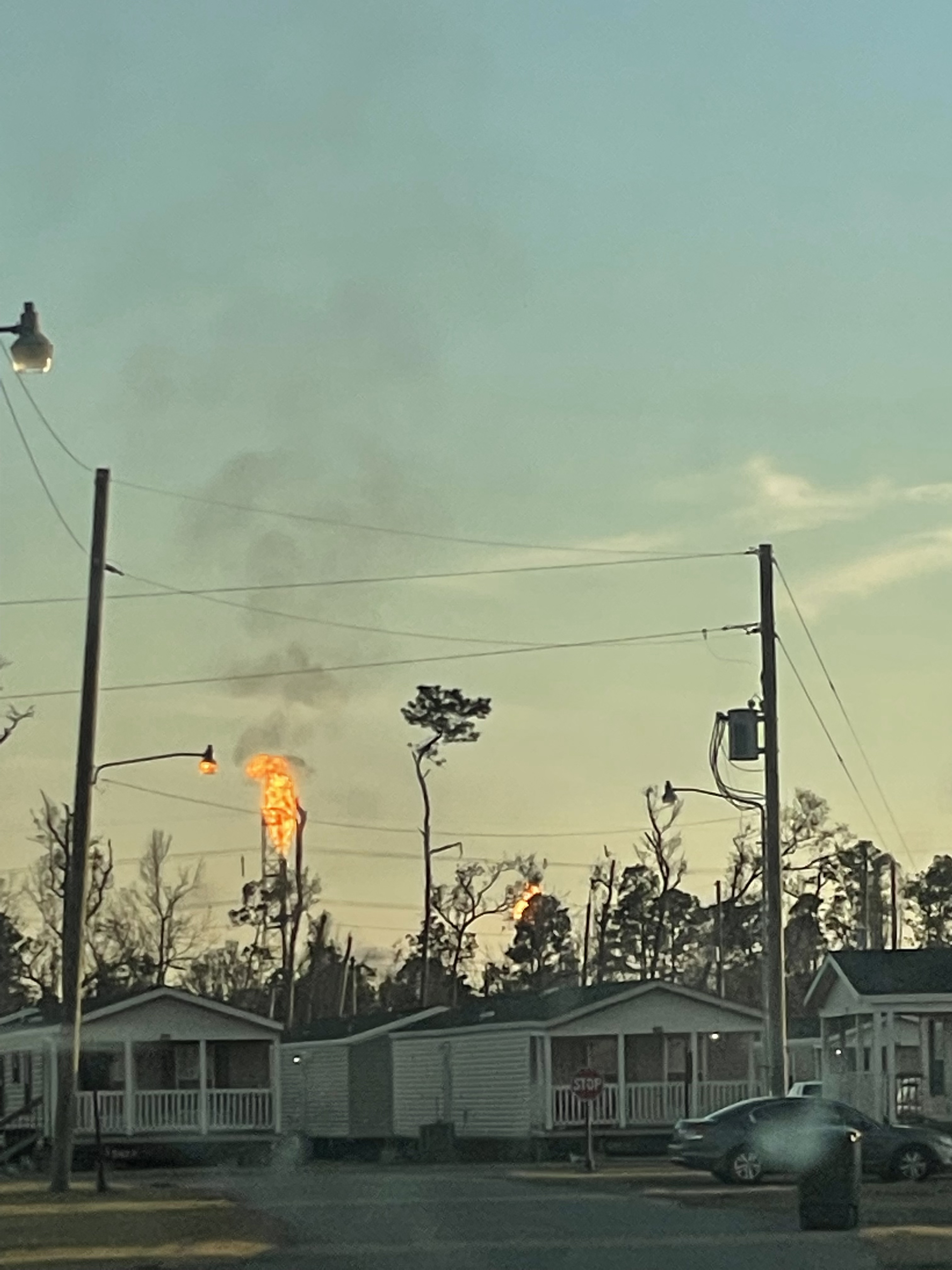 A flare and black smoke rise behind trailer homes