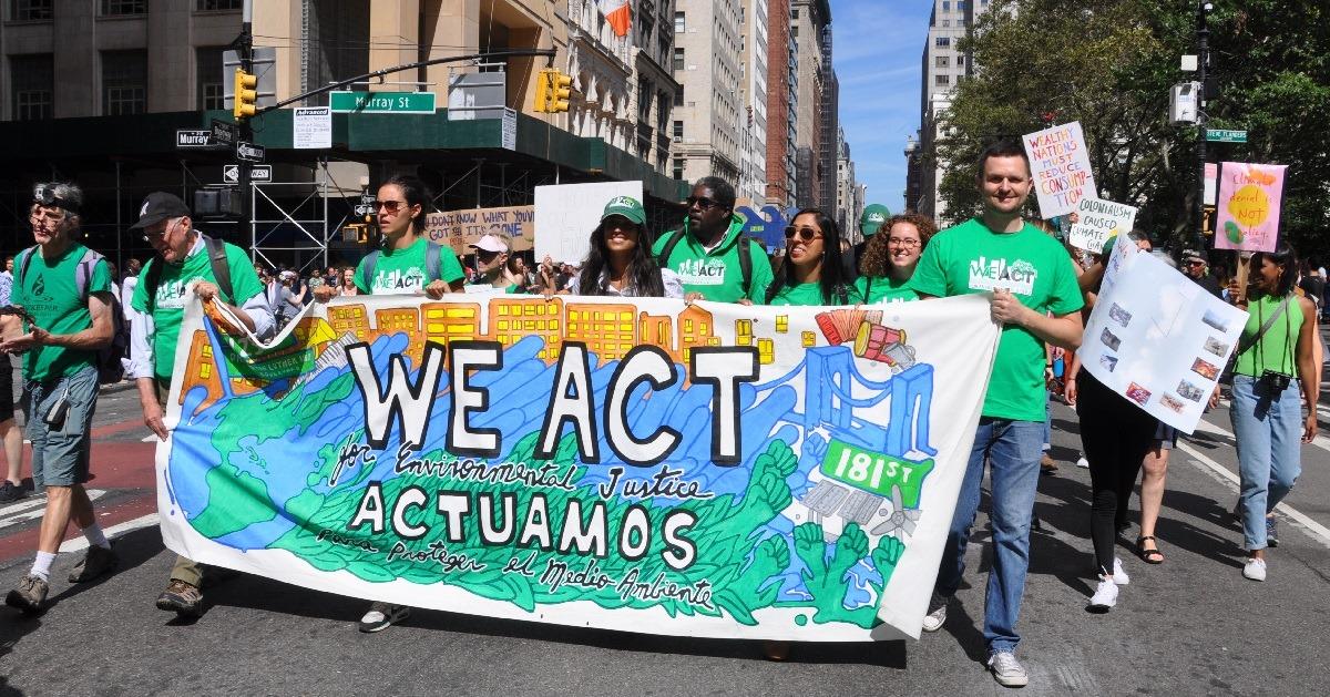 Protestors march holding a sign that reads "We Act for Environmental Justice"