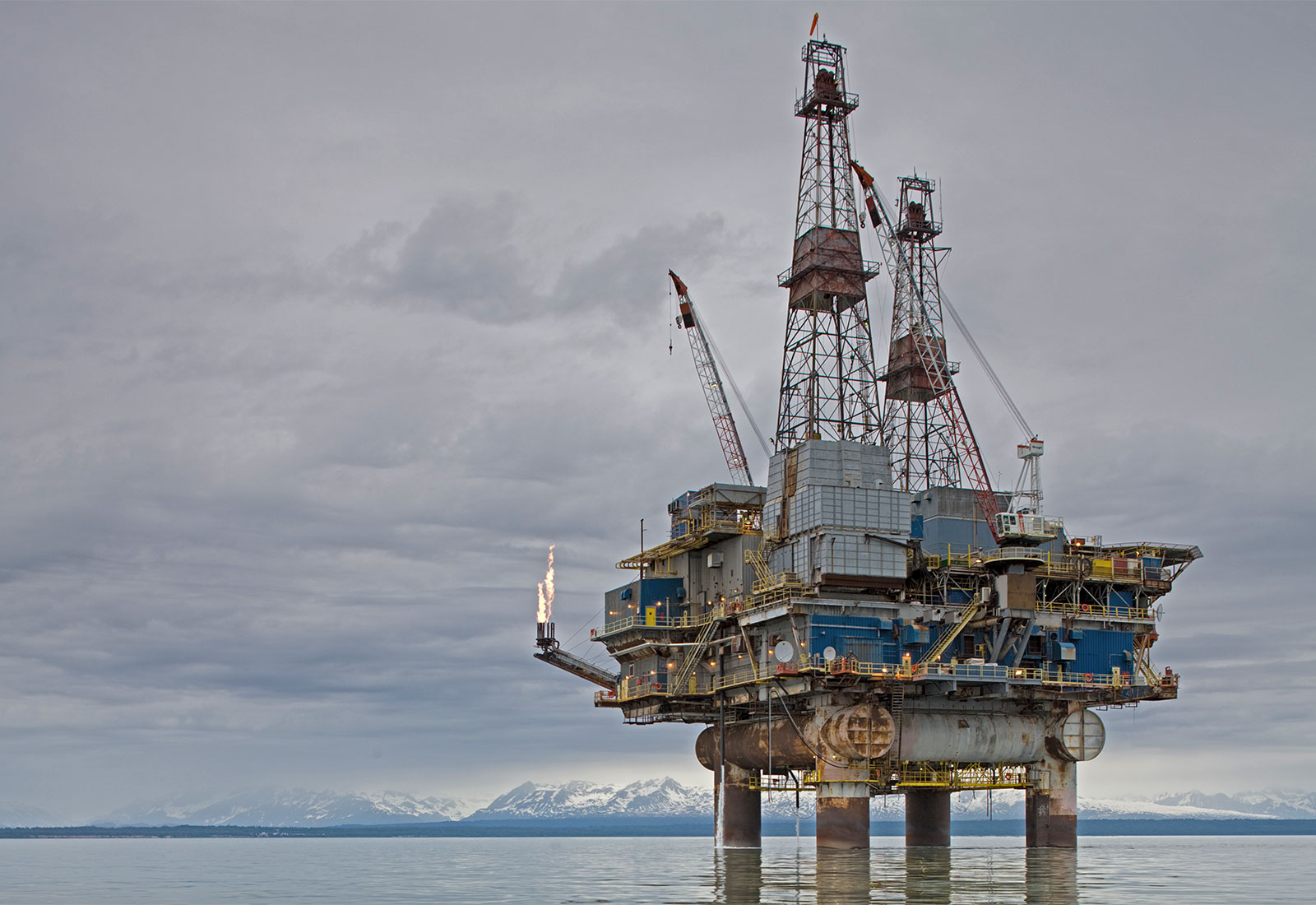 Offshore oil rig in water with Alaskan mountains in the distance