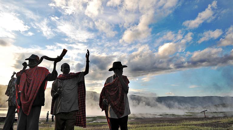 Four elders of the Endorois tribe, indigenous to Kenya, performing a ritual. Mist, mountains, and a blue sky with clouds are in the background