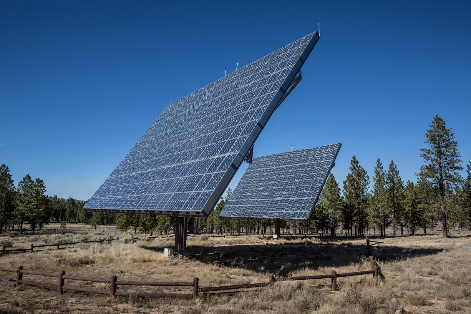 Two large solar panels are fenced in a dry, shrubby area.