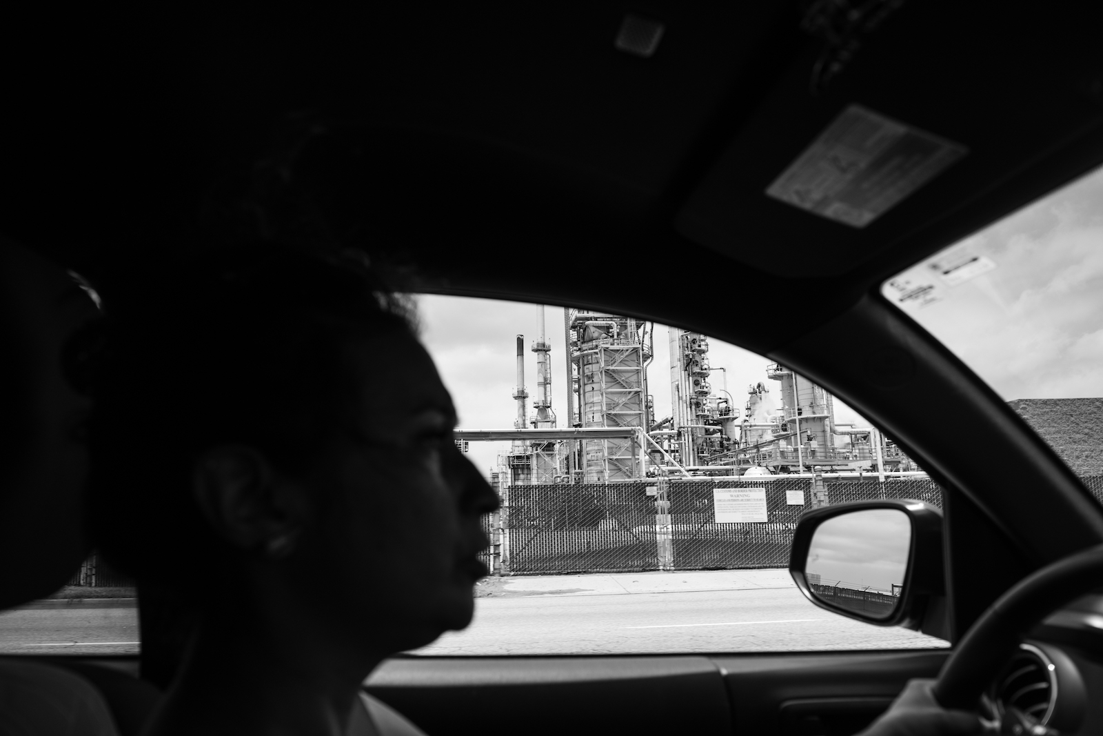 a woman in a car drives by a refinery