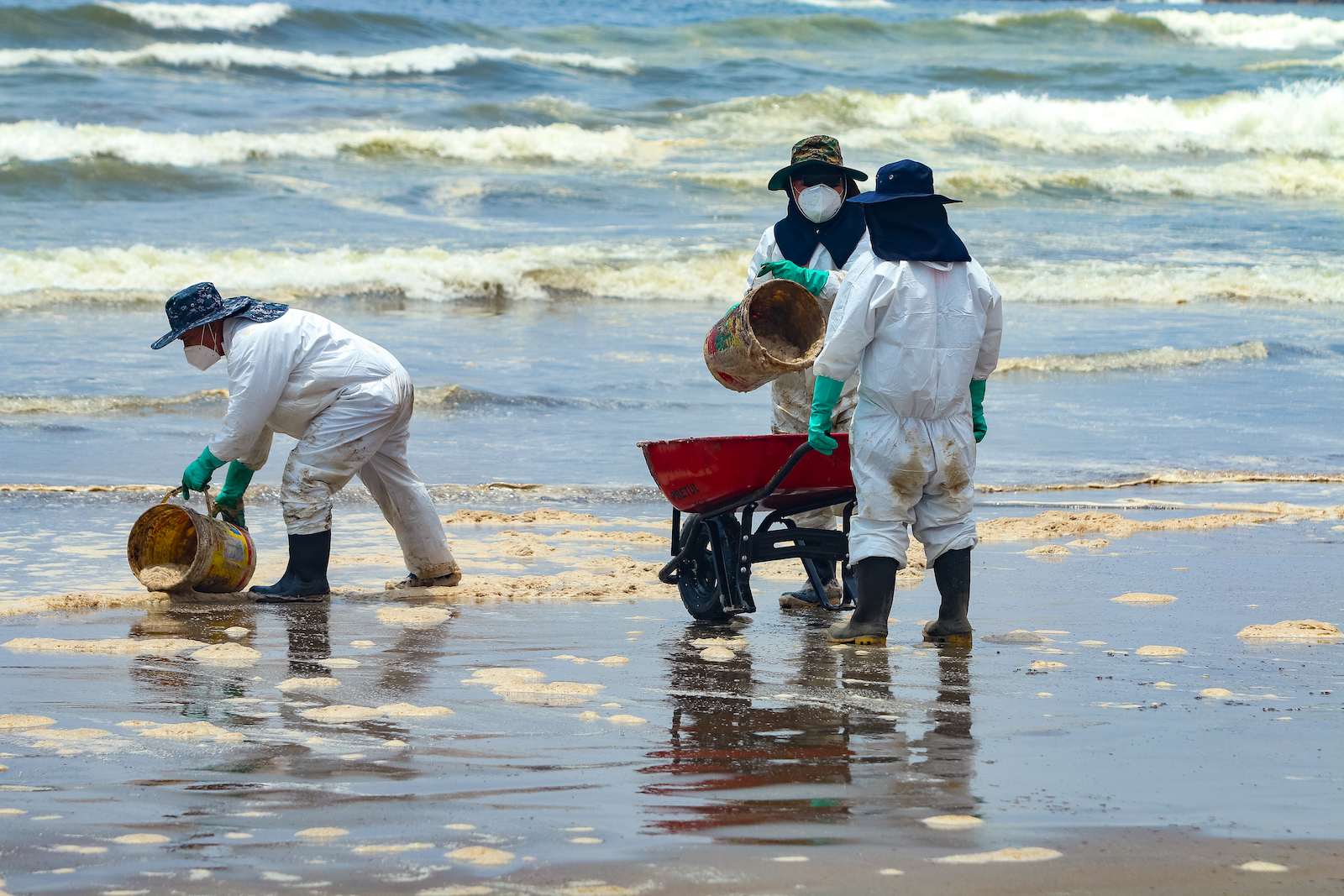 Repsol employees work filling buckets with contaminated sand during the cleanup in the shore of Cavero Beach on January 20, 2022 in Ventanilla, Peru.