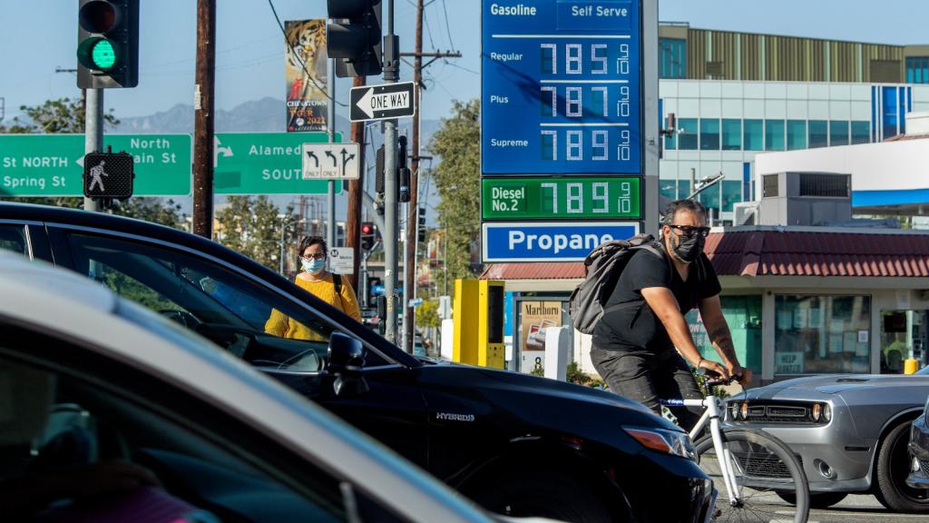 A busy street with cars and a biker in front of a gas station.