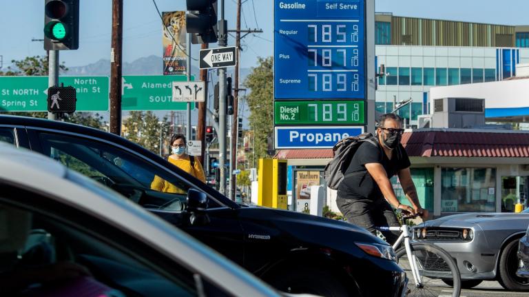 A busy street with cars and a biker in front of a gas station.