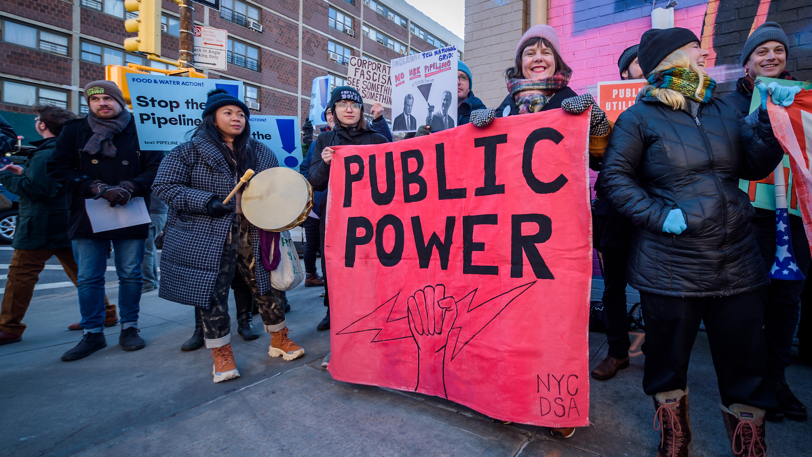 activists in new york hold a neon pink banner that says "Public Power"