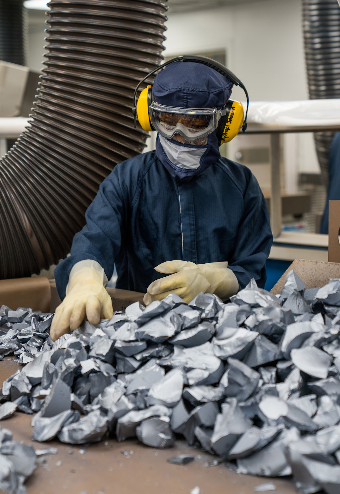 A person wearing a mask and headphones sorts polysilicon
