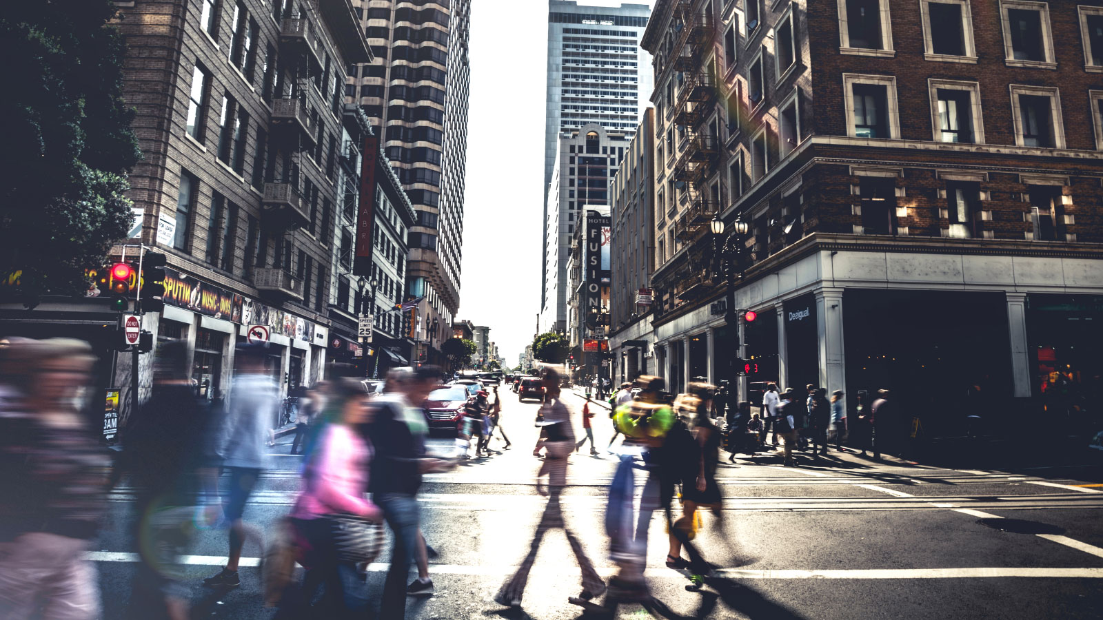 Motion-blurred people walking on a crosswalk with buildings on either side