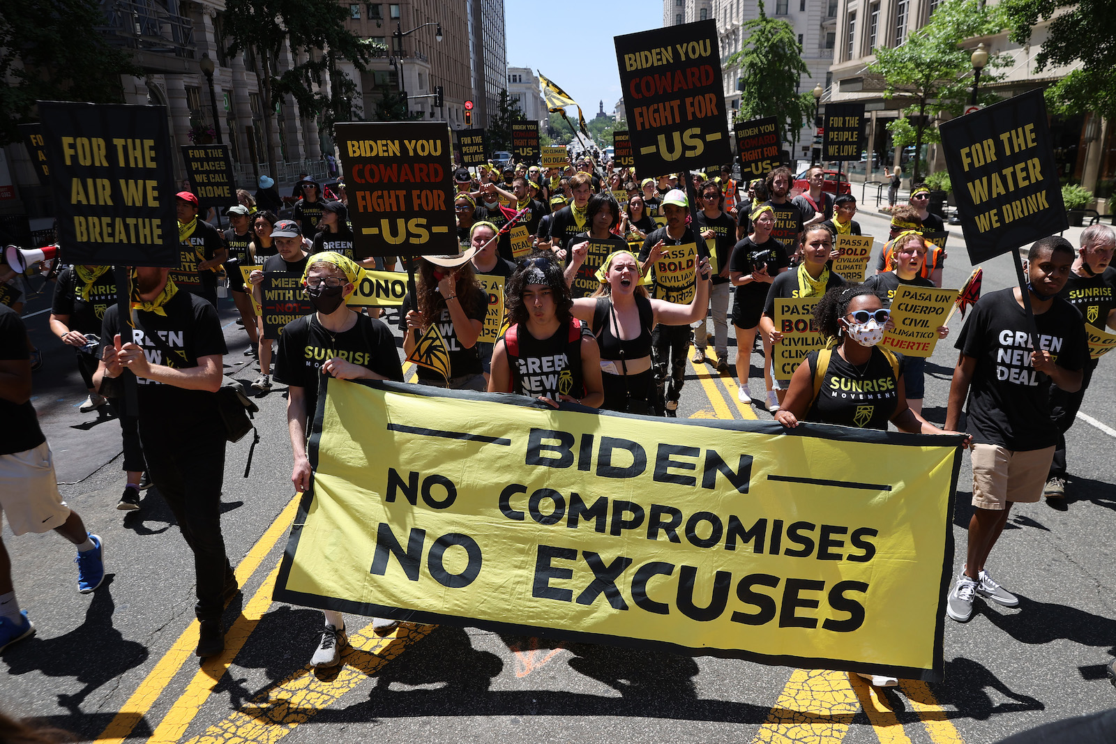 a large group of people march in the street holding a large yellow banner that says biden no compromises no excuses