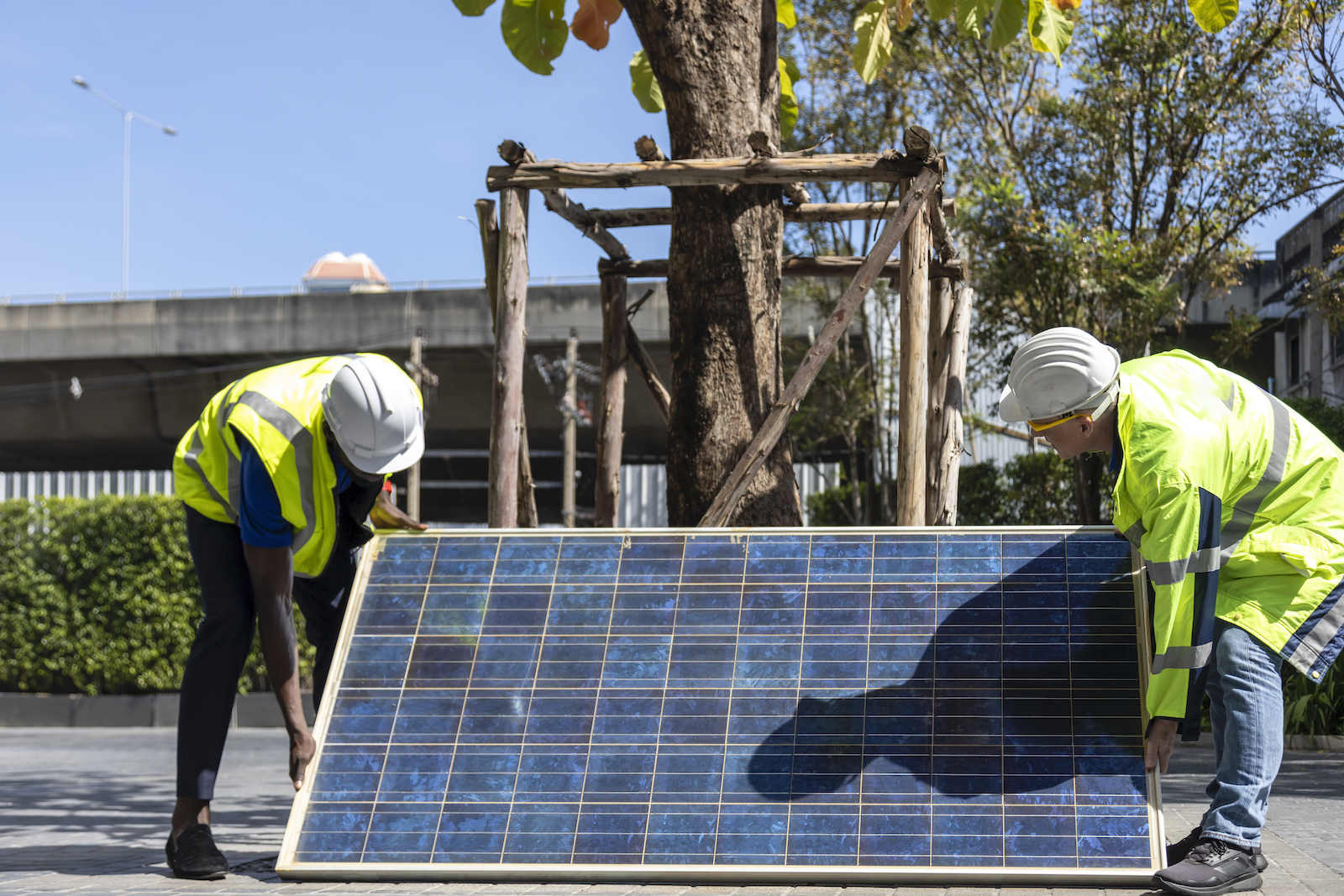 Two workers in reflective tops working on installing solar panel on the rooftop of the house