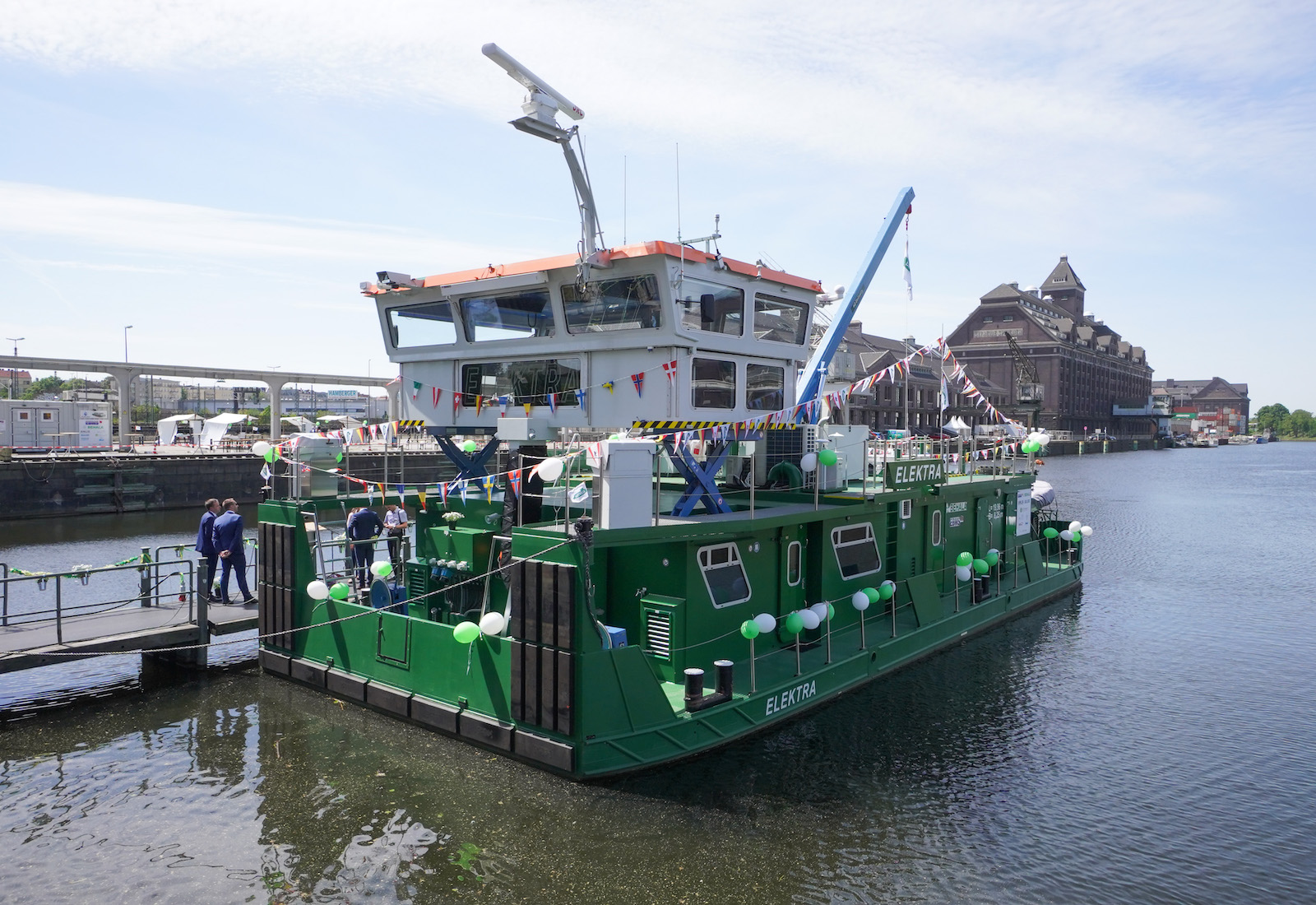 A green pushboat next to a pier