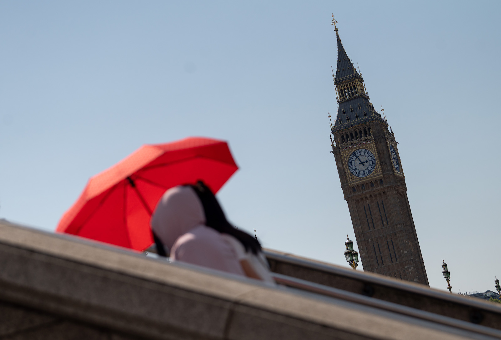 Two women walk along in front of the clock tower Big Ben with an umbrella as a sunshade.