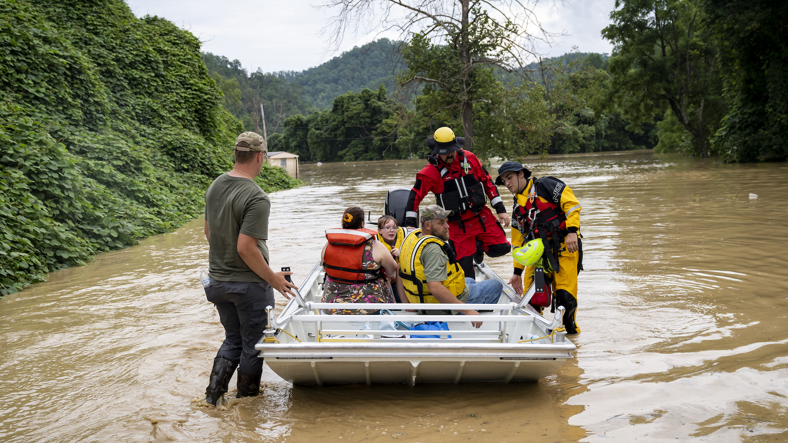 A group of people are rescued in a boat in muddy waters surrounded by mountains.
