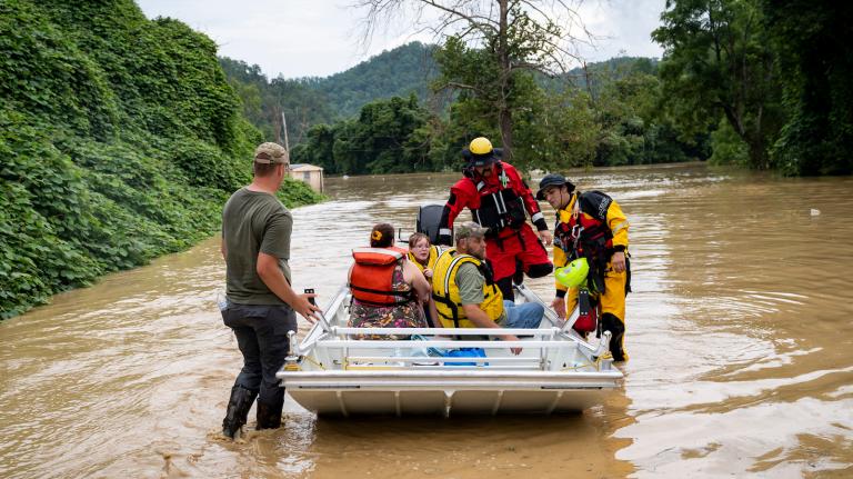 A group of people are rescued in a boat in muddy waters surrounded by mountains.