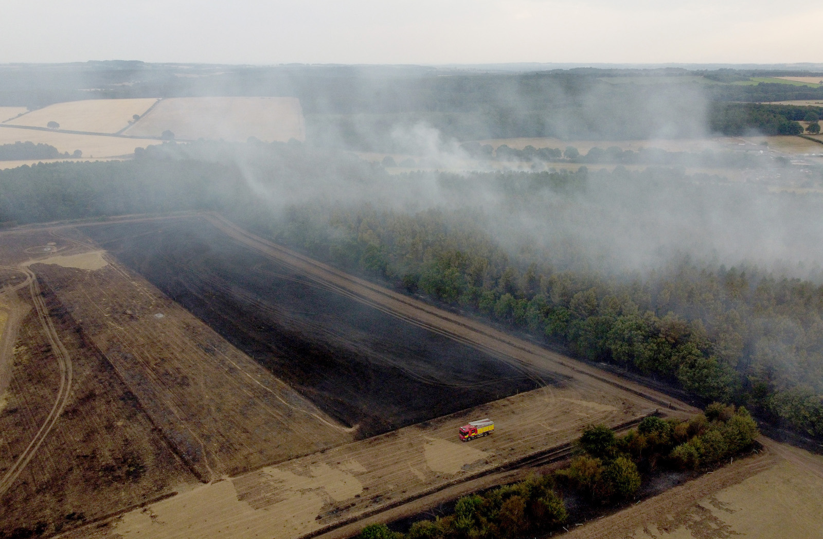In this aerial view, a fire engine is seen on the field while smoke rises from the trees on July 19, 2022 in Blidworth, England.