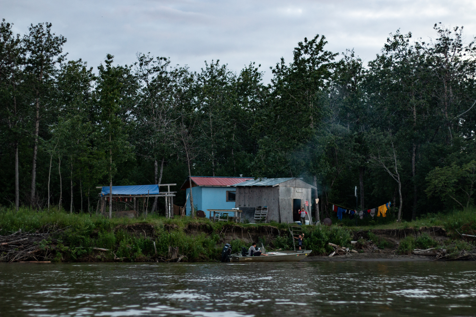 a small boat docks in front of a few small structures on the riverbank