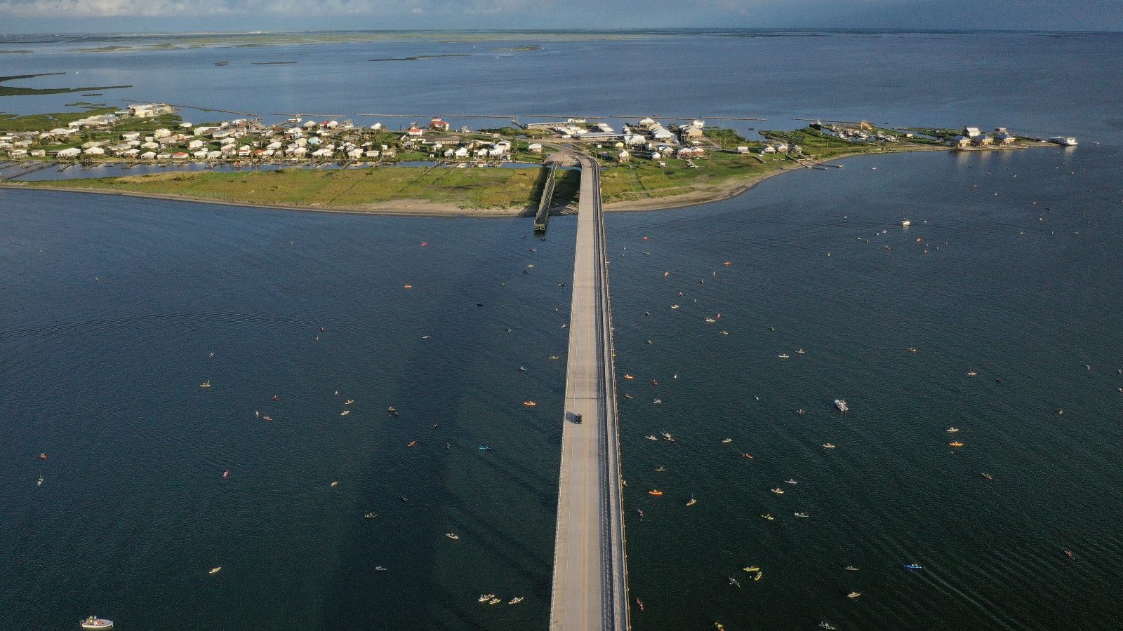 An aerial photo shows a long bridge leading to a small, precarious-looking island crowded with homes.