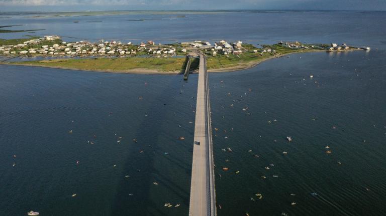 An aerial photo shows a long bridge leading to a small, precarious-looking island crowded with homes.