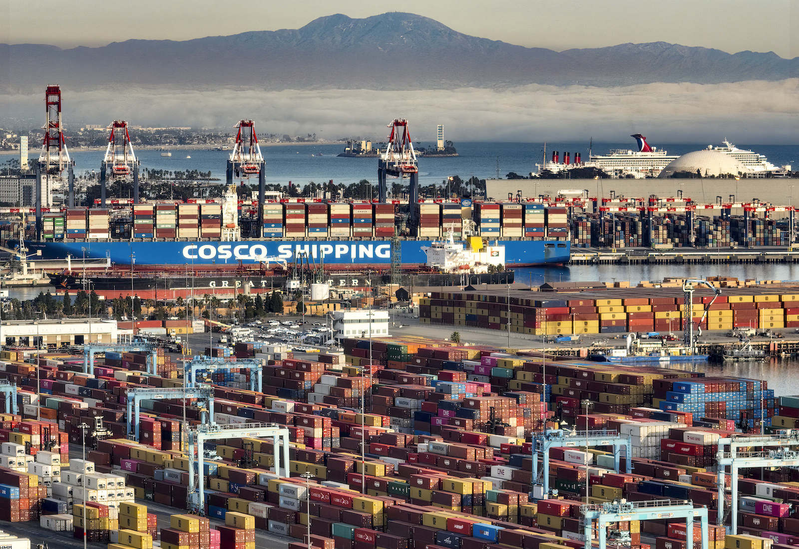 Containers are stacked up in the Port of Long Beach, with a mountain in the background