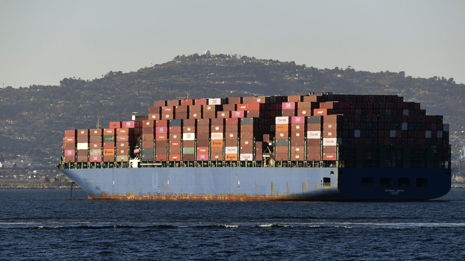 A large cargo ship on the ocean with a hill in the background