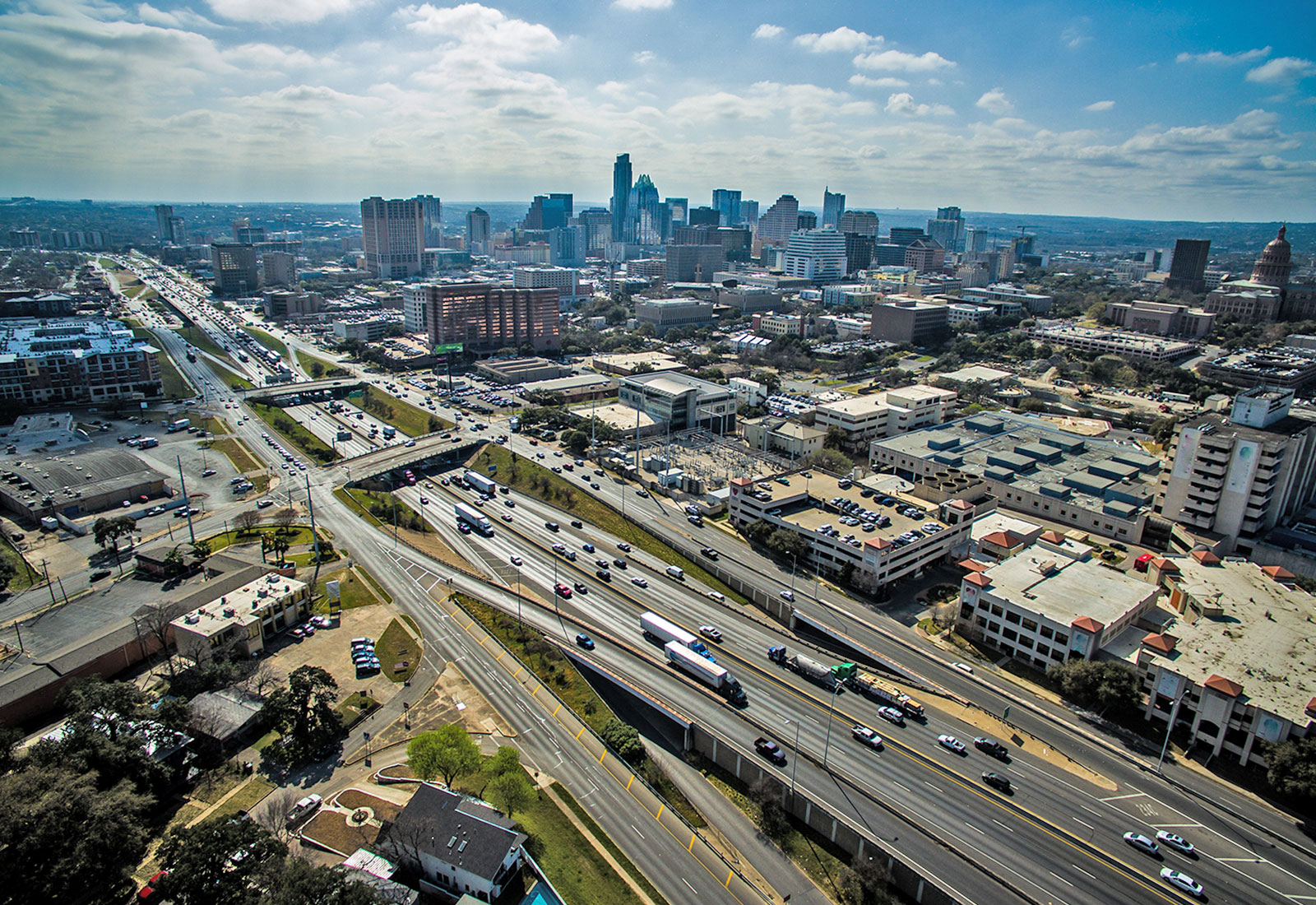 a major multiway highway with cars cuts across an urban area in front of the Austin skyline