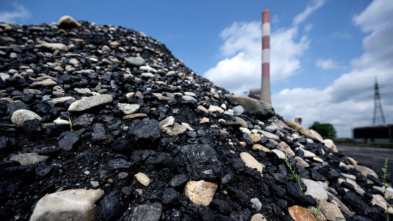 A large pile of coal and rocks with a coal power plant smokestack in the distance