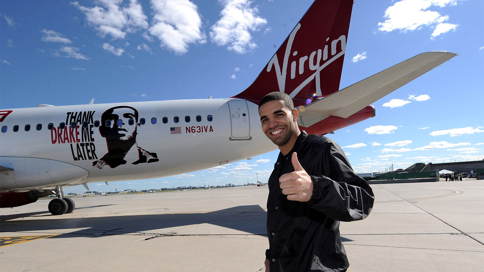 Musician Drake giving a thumbs up in front of a Virgin airlines plane with a decal of Drake's face and the words 